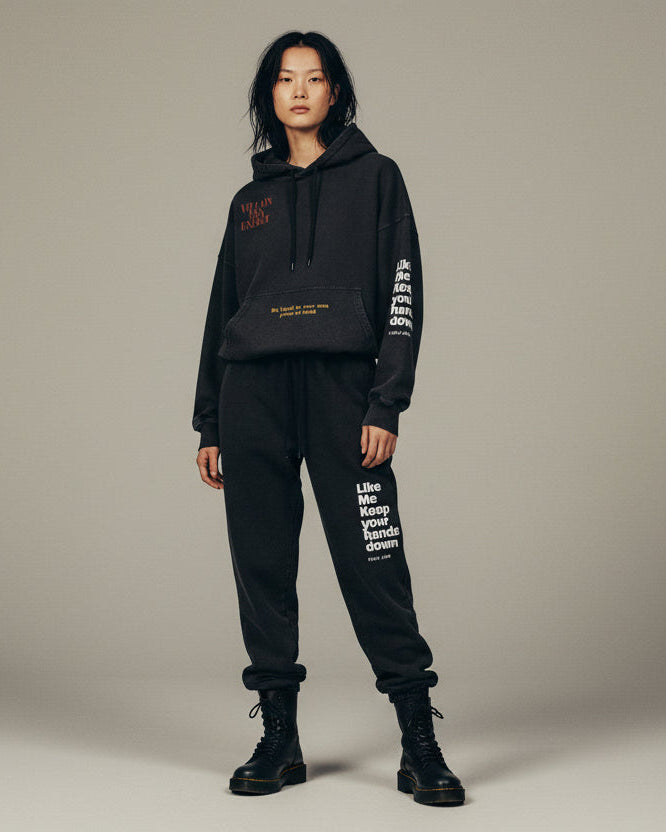 Person wearing a black hoodie and pants with text on a beige background