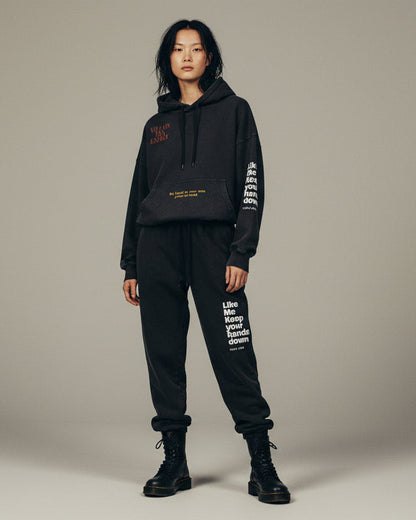 Person wearing a black hoodie and pants with text on a beige background