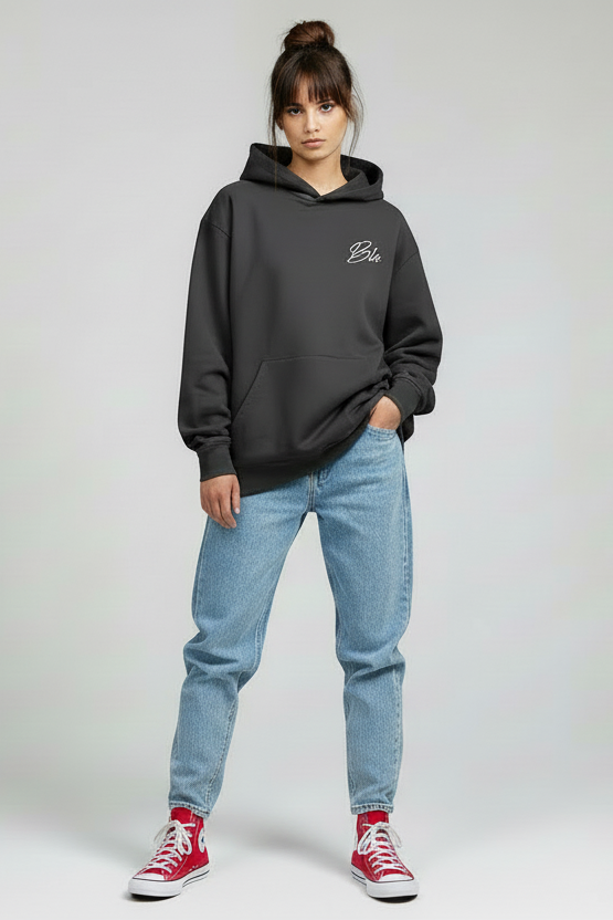 Person wearing a black hoodie with text, light blue jeans, and red sneakers on a plain background