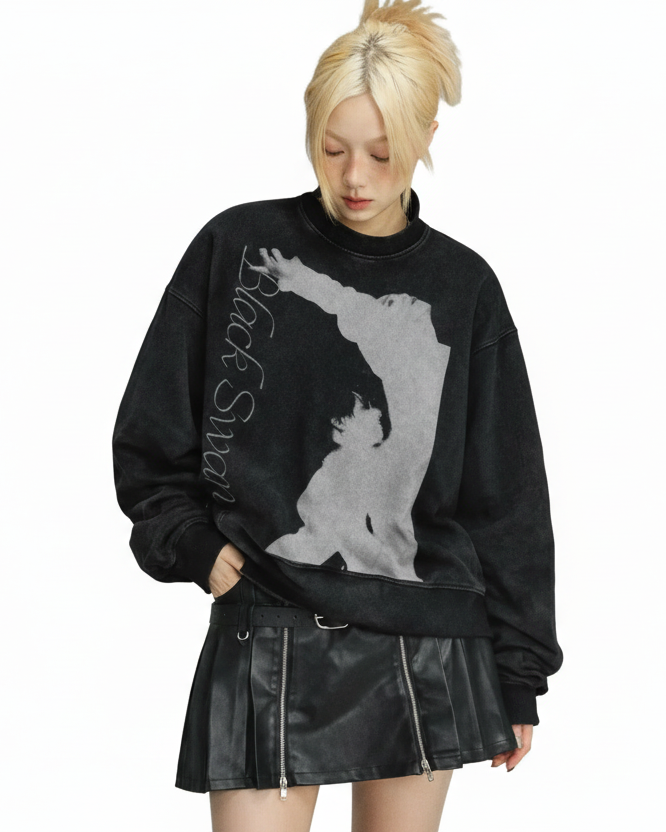 Person wearing a black sweatshirt with a graphic design and a leather skirt on a gray background