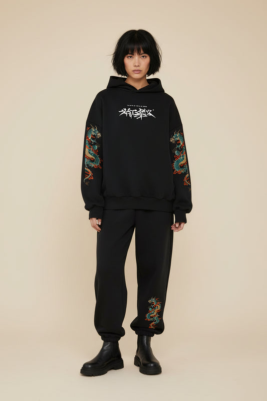 Person wearing a black hoodie and pants with dragon designs on a white background