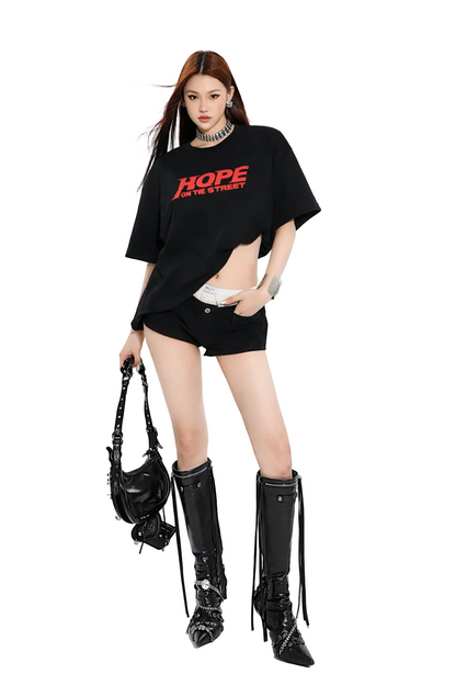 Person wearing a black oversized t-shirt with 'HOPE' text, black high-heeled boots, and holding a black handbag on a white background.