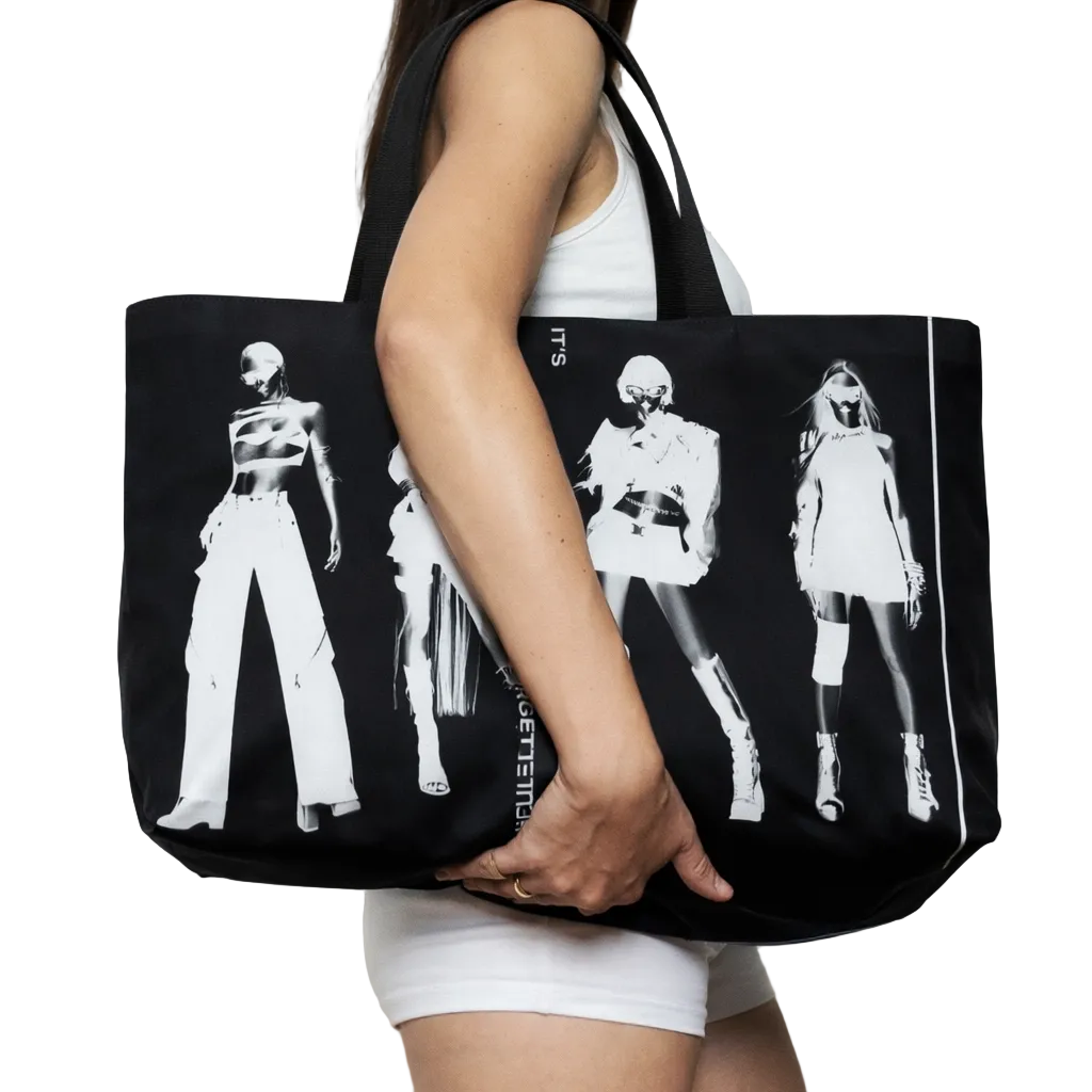 Person holding a black tote bag with white graphics on a plain background